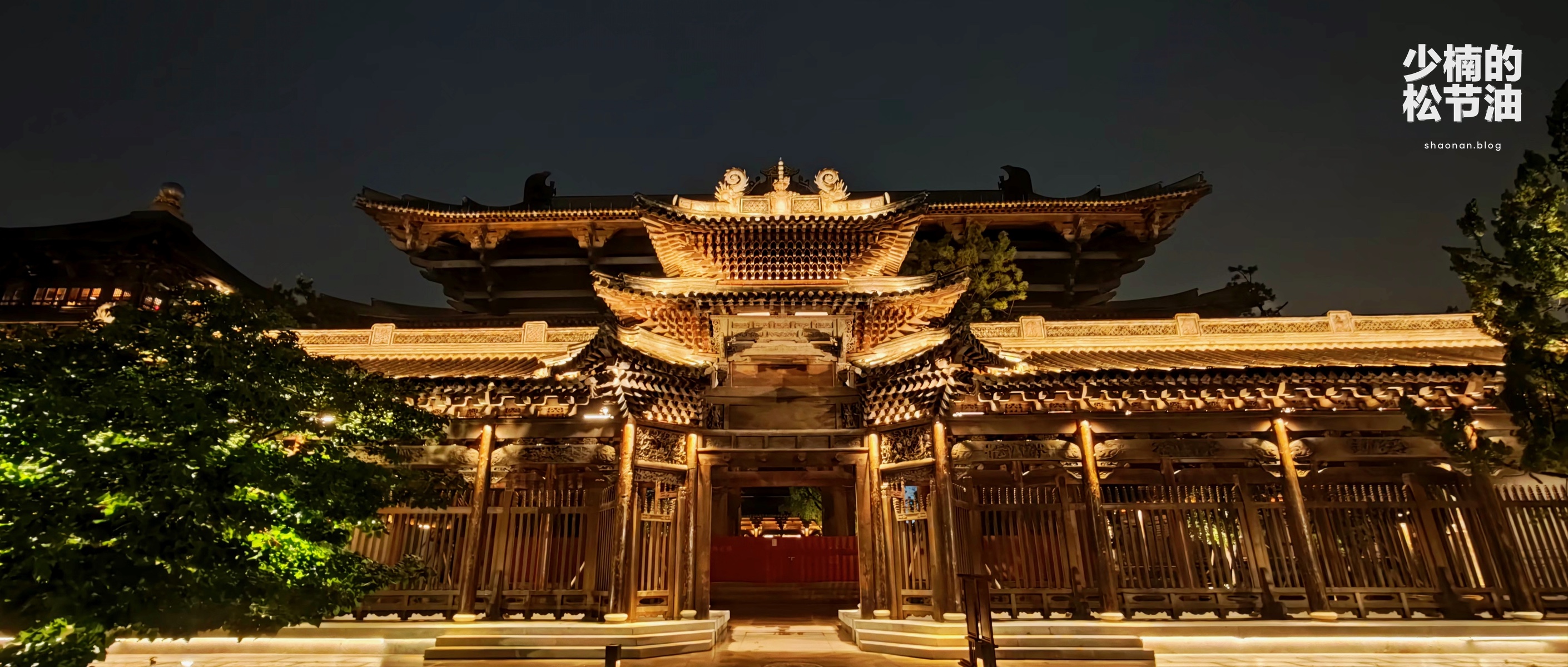 夜色中的古镇建筑，屋檐和木构被暖色灯光照亮。